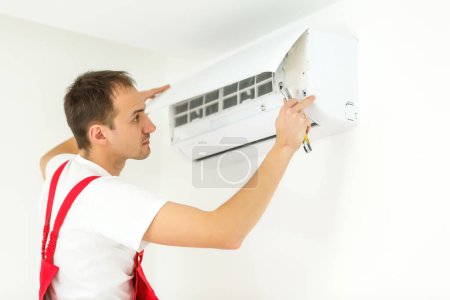Photo for Young worker installs air conditioner in the room with blue walls - Royalty Free Image