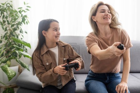 Photo for Photo of domestic funny blond lady mom daughter sitting comfy couch hold joystick playing video games stay home safety quarantine spend weekend together best friends living room indoors - Royalty Free Image