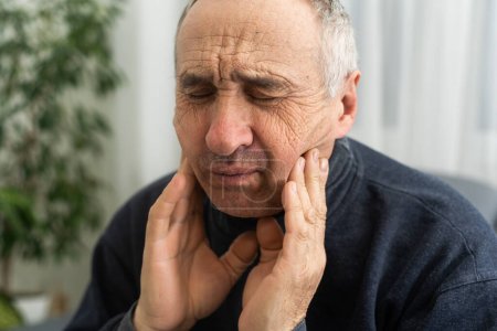 Photo for Old man with toothache. Elderly senior man has toothache. Unhappy man face in tooth pain sitting on sofa at home, feel sick unwell. Sad aged man hand holding his chin. Adult suffering toothache. - Royalty Free Image