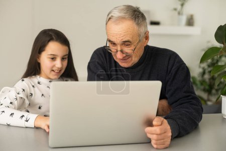 Grandfather and granddaughter spend time together use laptop, browse website, younger generation teach explain to older how to use modern tech concept.