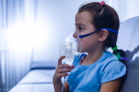 Téléchargez les photos : Petite fille caucasienne respire avec un masque spécial, qui aide à arrêter la crise d'asthme ou à soulager les symptômes de la maladie respiratoire. - en image libre de droit