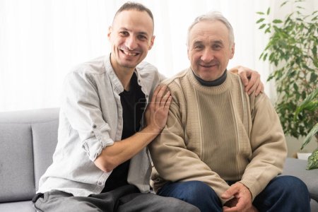 Photo for Happy two generations male family old senior mature father and smiling young adult grown son enjoying talking chatting bonding relaxing having friendly positive conversation sit on sofa at home - Royalty Free Image