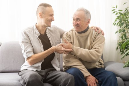 Photo for Happy two generations male family old senior mature father and smiling young adult grown son enjoying talking chatting bonding relaxing having friendly positive conversation sit on sofa at home - Royalty Free Image