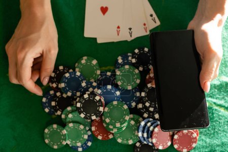 joueur de poker en ligne avec un smartphone à une table de casino avec des cartes et des jetons