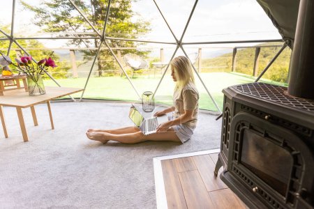 Téléchargez les photos : Joyeux jeune femme bavarder en ligne en utilisant un ordinateur portable dans le camping dôme. Glamping concept de vacances. - en image libre de droit