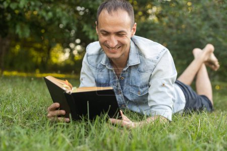Photo for A man reads the Bible on the grass at a park. - Royalty Free Image