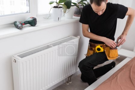 Photo for Man is repairing radiator battery in the room. Maintenance repair works renovation in the flat. Heating restoration. Wrench in hands. High quality photo - Royalty Free Image