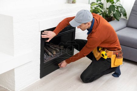 Téléchargez les photos : Professional technician sealing electric fireplace with caulk near white wall in room. - en image libre de droit