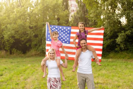 Téléchargez les photos : Famille heureuse avec le drapeau de l'Amérique États-Unis au coucher du soleil en plein air. - en image libre de droit
