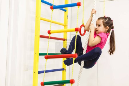 Téléchargez les photos : Children Activity Concepts. Little Caucasian Girl Having Stretching Exercises on Wall Bars Indoors - en image libre de droit