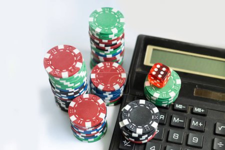 Vue du haut vers le bas sur la calculatrice entourée de jetons de poker blancs, bleus et verts sur fond blanc. Comprend espace de copie
