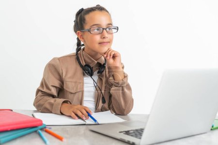 Téléchargez les photos : E-Learning. Choqué petite écolière regardant ordinateur portable portant des écouteurs regardant la caméra Web de l'ordinateur dans le choc de faire appel vidéo et d'apprendre en ligne à la maison. Shocking News Concept - en image libre de droit