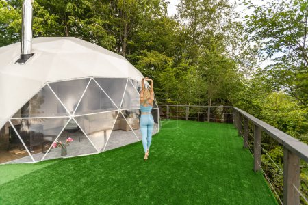 Téléchargez les photos : A woman is doing exercises on the terrace of a transparent bubble dome. - en image libre de droit