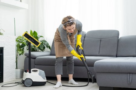 Photo for Woman cleaning couch with vacuum cleaner at home. - Royalty Free Image