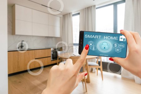 Hand of woman holding smartphone in blurred kitchen with double exposure of smart home interface. Concept of automation