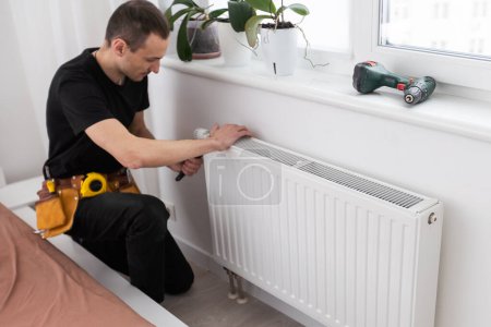 Photo for Man is repairing radiator battery in the room. Maintenance repair works renovation in the flat. Heating restoration. Wrench in hands. High quality photo - Royalty Free Image