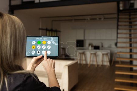 Téléchargez les photos : Young woman using smart home app to control light turning on with tablet pc. - en image libre de droit
