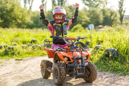 Photo for The little girl rides a quad bike. A mini quad bike is a cool girl in a helmet and protective clothing. Electric quad bike electric car for children popularizes green technology - Royalty Free Image
