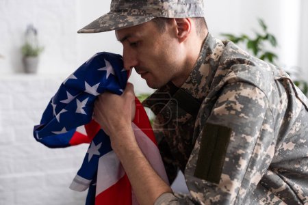 Photo for Upset American soldier holding flag of United States while crying during memorial day. - Royalty Free Image