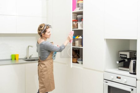 Attractive woman cleaning furniture in kitchen with a rag.