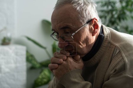 Photo for Please, Lord. Nervous worried aged Caucasian man praying on couch at home. Stressed white European senior citizen sitting on sofa, begging for forgiveness or asking God for help in difficult situation - Royalty Free Image