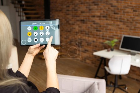 Téléchargez les photos : Young woman using smart home app to control light turning on with tablet pc. - en image libre de droit