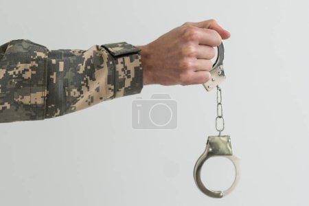 Photo for A military man in handcuffs holds an army badge in his hand on a dark background, selective focus. Concept: war criminal, prisoner of war, tribunal for deserters, traitor to the Motherland. - Royalty Free Image
