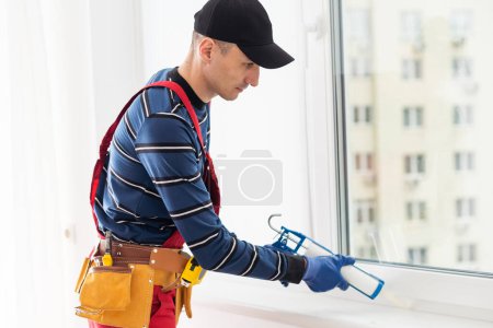 Téléchargez les photos : Ouvrier de la construction étanchéité fenêtre avec calfeutrage intérieur
. - en image libre de droit