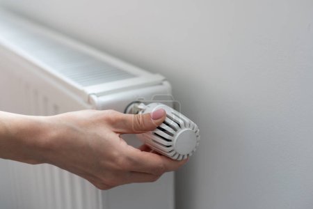 Una mano de mujer sostiene la manija del termostato de calefacción. concepto de costo de servicio de calefacción, aumento de precio de utilidad. Foto de alta calidad