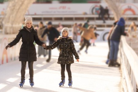 Mother with her daughters skates on ice skating.