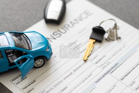 Top view of car insurance claim form with car key and car toy on desk.