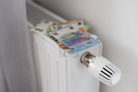 Téléchargez les photos : Nouveau thermostat avec Euro cash sur un radiateur chauffant à la maison. Coûts de chauffage coûteux image symbolique. Photo de haute qualité - en image libre de droit