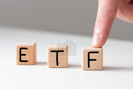 Text-ETF auf Holzwürfeln auf weißem texturiertem Kitt-Hintergrund. Abkürzung für Exchange Traded Funds. Quadratische Holzblöcke. Draufsicht, flache Lage. Hochwertiges Foto