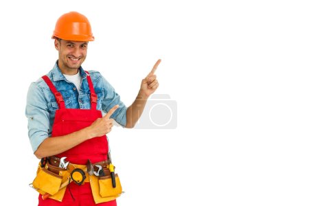 Foto de Cheerful male contractor wearing helmet isolated on white background pointing aside while looking at camera. - Imagen libre de derechos