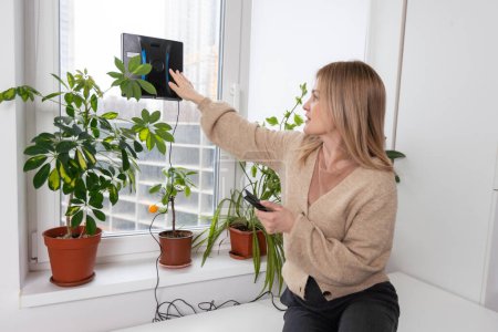 Téléchargez les photos : Aspirateur robot nettoyage fenêtre dans le haut bâtiment extérieur. jeune femme contrôle la télécommande - en image libre de droit
