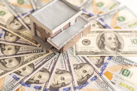 Defokussierter Blick auf das Modell eines Holzhauses auf dem Hintergrund von US-Dollarnoten. Wohnungsmarkt, Versicherung, Kauf oder Vermietung von Immobilien. Hochwertiges Foto
