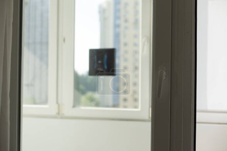 Téléchargez les photos : Robot de lavage de fenêtre moderne effectue un travail sur une fenêtre sale. Nettoyage de la maison avec des appareils intelligents. Robot de nettoyage automatique des vitres, femme de ménage. Photo de haute qualité - en image libre de droit