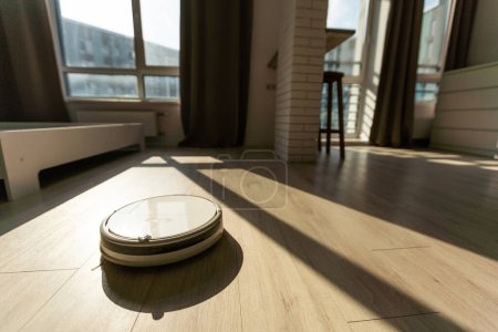 Photo for Robotic vacuum cleaner on laminate wood floor in living room. - Royalty Free Image