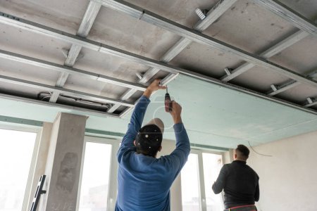 Téléchargez les photos : Installation de plafond avec des techniciens experts Dans la pièce qui est dans le processus de construction. Photo de haute qualité - en image libre de droit
