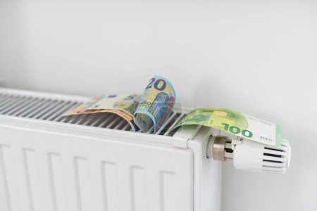 Téléchargez les photos : Billet de banque couché sur le radiateur, le concept de hausse des prix de l'énergie et de chauffage plus cher. Photo de haute qualité - en image libre de droit