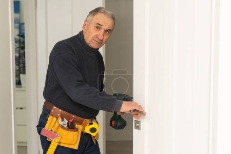 Foto de Ordinary elderly man independently repairs a door. - Imagen libre de derechos