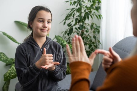 Photo for Daughter talk with middle aged mother people using sign language, family sitting on armchair side view, teacher teach teenager deaf-mute girl to visual-manual gestures symbols concept image. - Royalty Free Image