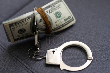 Police handcuffs lie on a lot of dollar bills. The concept of illegal possession of money, illegal transactions with US dollars. Economic Crime. High quality photo