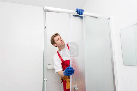 Téléchargez les photos : Plombier utilisant une cartouche en silicone pour fixer le batten en aluminium de la cabine de douche
. - en image libre de droit