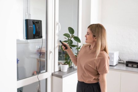 Téléchargez les photos : Femme nettoyage des fenêtres à la maison avec nettoyant robotique - en image libre de droit