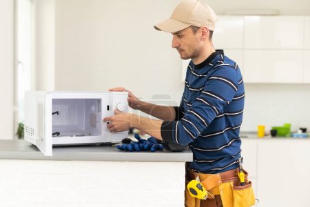 Photo for Young repairman fixing and repairing microwave oven - Royalty Free Image