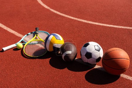Una variedad de equipos deportivos que incluyen un fútbol americano, una pelota de fútbol, una raqueta de tenis, una pelota de tenis y una pelota de baloncesto.