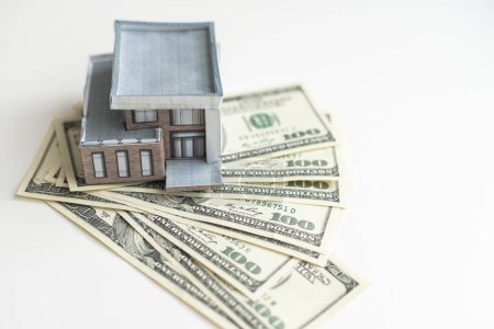 Photo for A small house lies on a fan of hundred dollar bills. The keys to the purchased house. Reduced copy of the house on a white background. High quality photo - Royalty Free Image
