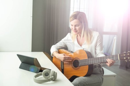 Foto de Mujer joven y serena en auriculares inalámbricos usando un instrumento musical acústico mientras está sentada con una computadora portátil. Foto de alta calidad - Imagen libre de derechos