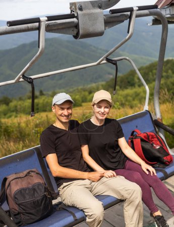 Man and a woman riding on the lift down the scenic Mountain during summer. Green tree forest surrounds the escalator